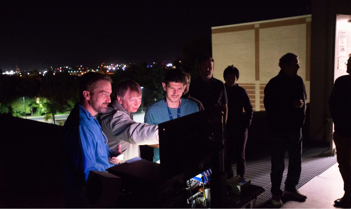 Members of the AWE research team gathered around a computer monitor on a rooftop at night.