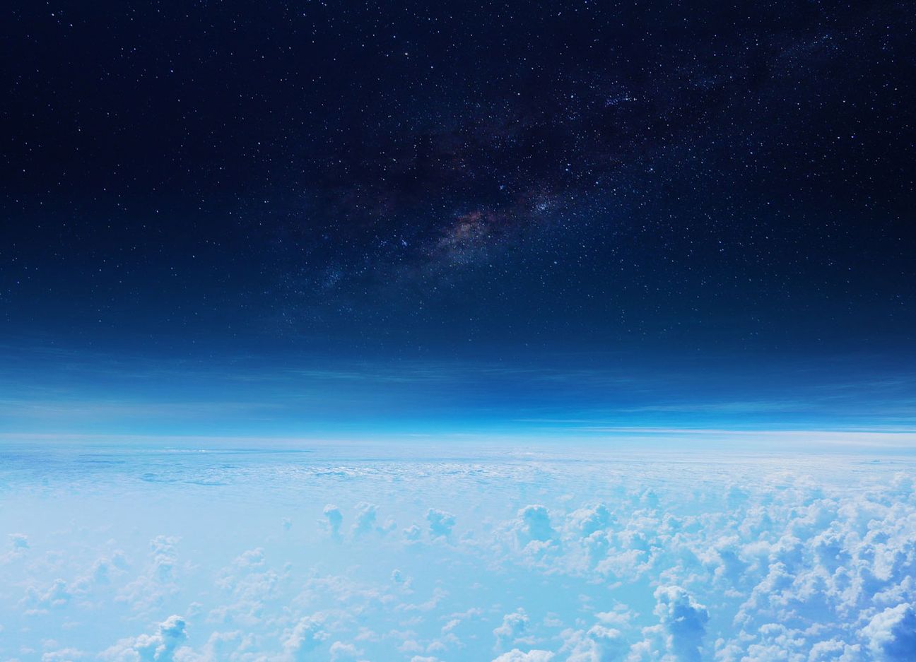 A view of the stratosphere from space. Clouds below, a hazy blue line and then the darkness of space with stars.