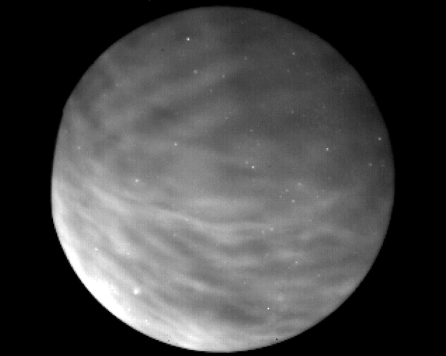 The whole Earth is shown in greyscale with white and grey lines of atmospheric gravity waves hovering above it.